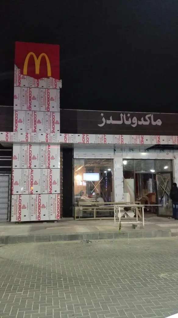 واجهة مطعم أثناء تلبيسها بألواح الكابوند مع عمود إعلاني (بايلون) يحمل الشعار، والحماية اللاصقة لم تُنزع بعد.